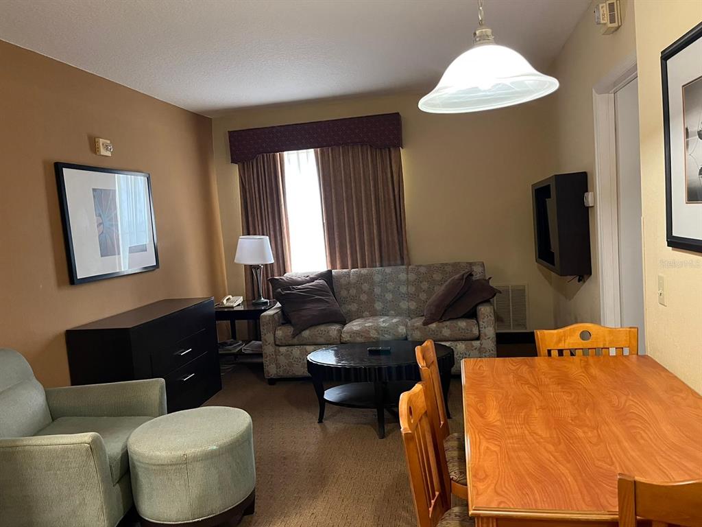 A hotel-style living area features a sofa, armchair, dining table, and dark wood furniture — 7601 CANADA AVENUE UNIT 418, ORLANDO, FL