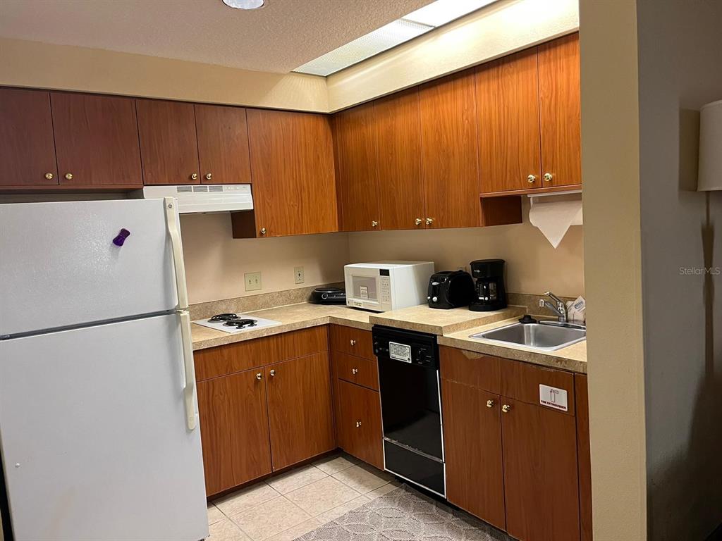 A kitchen with wood cabinets, laminate countertops, a white refrigerator, and a small sink — 7601 CANADA AVENUE UNIT 418, ORLANDO, FL