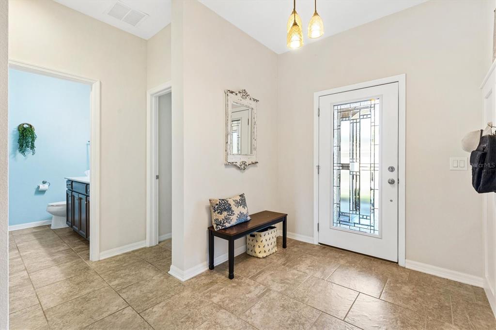 A tiled entryway features a white front door, a wooden bench, and a wall mirror — 4110 ARLINGTON RIDGE BOULEVARD, LEESBURG, FL