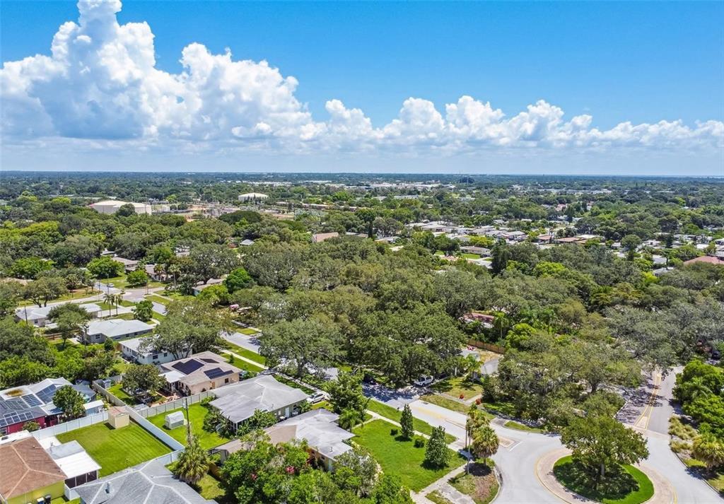 An aerial view shows a suburban neighborhood with houses, lush green trees, and a cul-de-sac — 210 BAKER AVENUE, CLEARWATER, FL