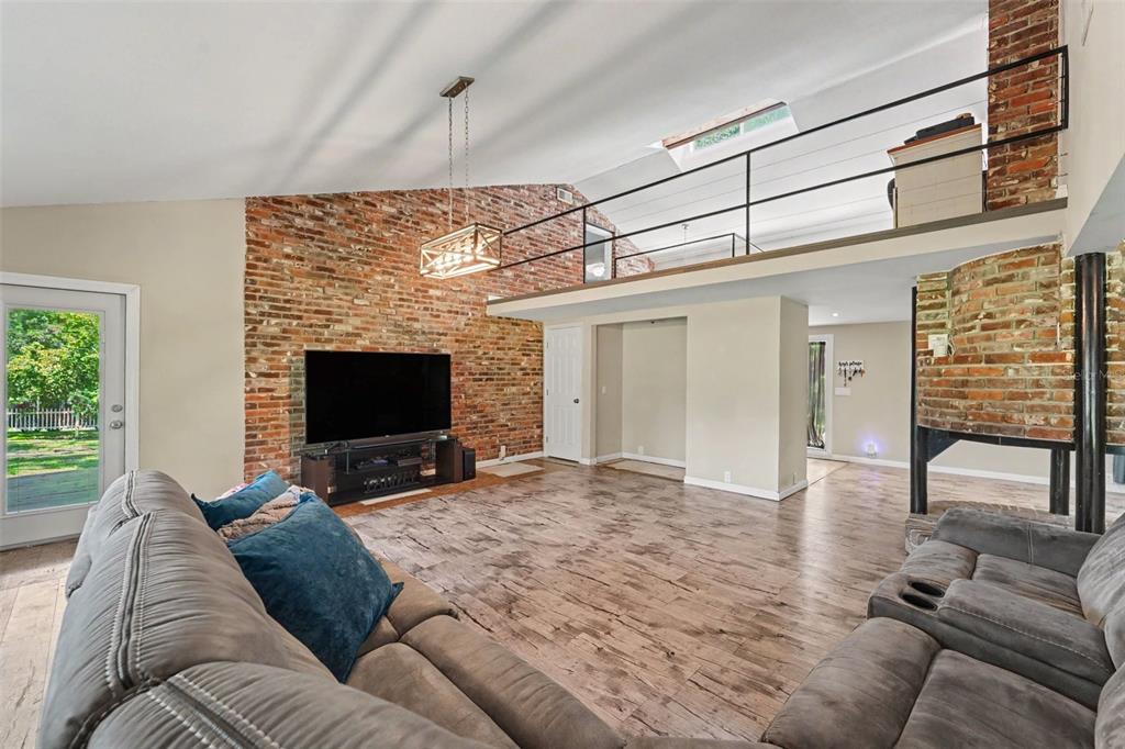 A living room features a brick accent wall, vaulted ceiling, loft area, and wood-look flooring — 434 HAMLIN WAY, BROOKSVILLE, FL