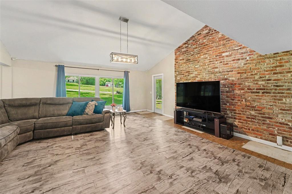 A living room features a vaulted ceiling, wood-look flooring, and a large brick accent wall — 434 HAMLIN WAY, BROOKSVILLE, FL