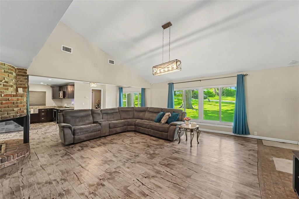A spacious living room features a vaulted ceiling, wood-look flooring, a brick fireplace, and sectional — 434 HAMLIN WAY, BROOKSVILLE, FL