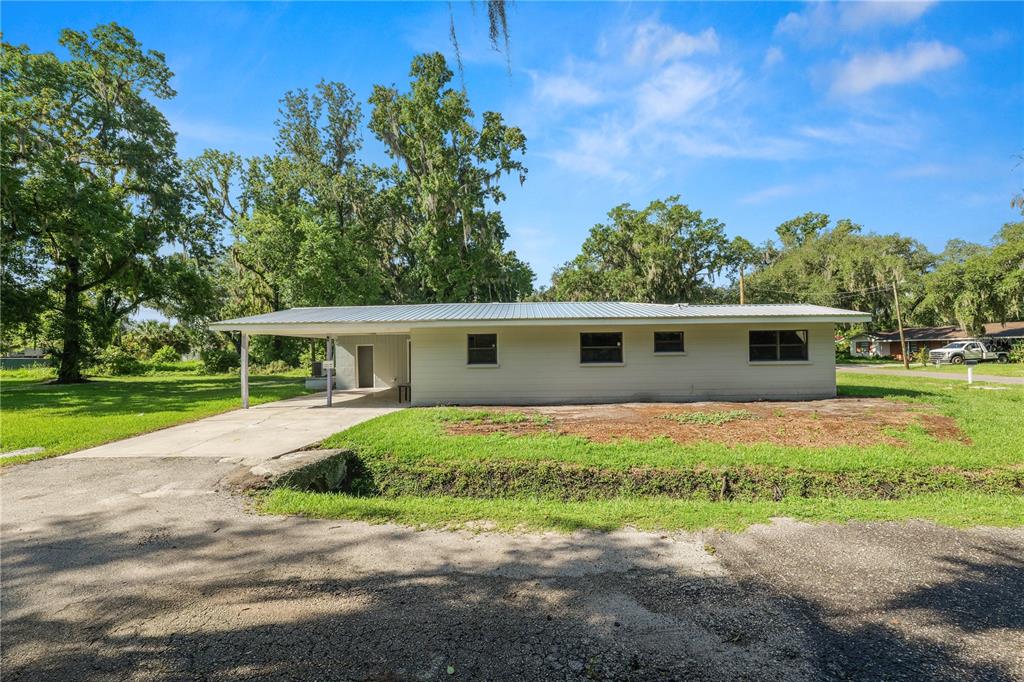 A single-story house with a metal roof and an attached carport sits on a lawn — 1112 N PENNSYLVANIA AVENUE, PLANT CITY, FL