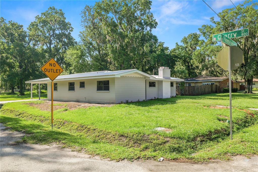 A single-story house with a white exterior and a chimney sits on a grassy corner lot — 1112 N PENNSYLVANIA AVENUE, PLANT CITY, FL