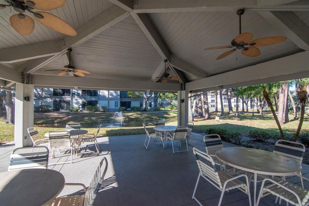 A covered outdoor patio features multiple dining tables, ceiling fans, and a view of a pond — 2650 COUNTRYSIDE BOULEVARD UNIT F303, CLEARWATER, FL