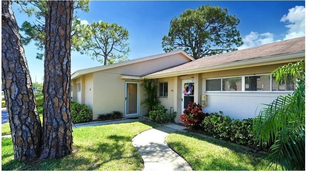A single-story house exterior with a concrete walkway, pine trees, and a landscaped front yard — 2782 WOODGATE LANE UNIT 12, SARASOTA, FL