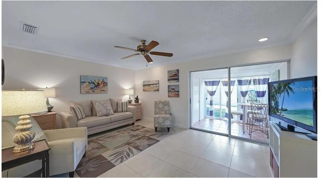 A living room features a beige sofa, patterned rug, ceiling fan, and sliding glass doors — 2782 WOODGATE LANE UNIT 12, SARASOTA, FL