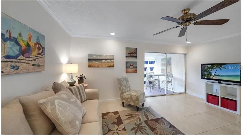 A living room features a beige sofa, patterned accent chair, area rug, and sliding glass doors — 2782 WOODGATE LANE UNIT 12, SARASOTA, FL
