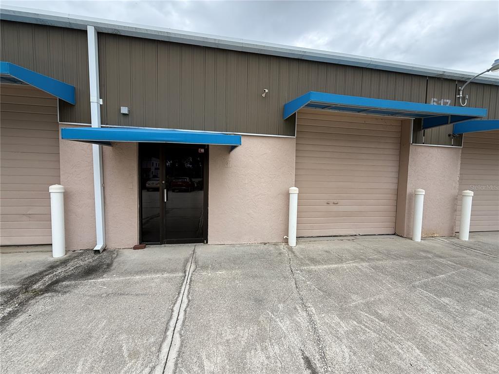 The exterior of a commercial building features a glass entrance door and two roll-up doors — 517 PAUL MORRIS DRIVE UNIT B4, ENGLEWOOD, FL
