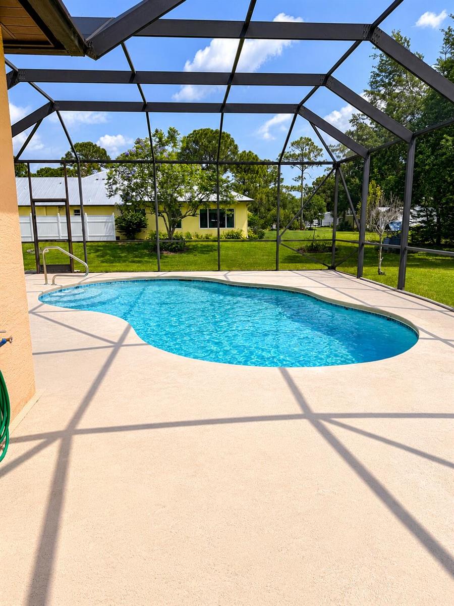 A swimming pool with a screen enclosure sits on a patio behind a yellow house — 5508 Silver Oak Drive, Fort Pierce FL 34982, FORT PIERCE, FL