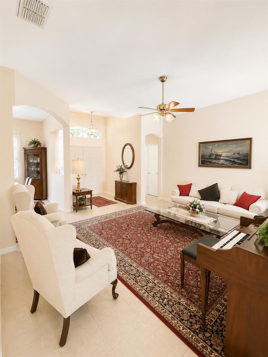 A living room features a large red patterned rug, cream-colored furniture, and a ceiling fan — 5508 Silver Oak Drive, Fort Pierce FL 34982, FORT PIERCE, FL
