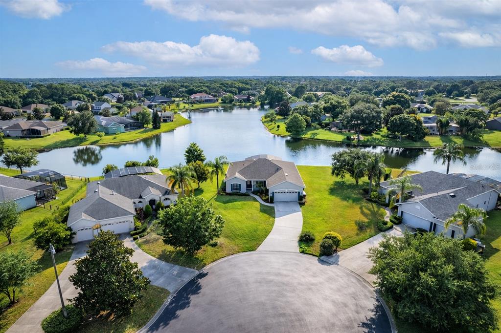 An aerial view shows a suburban house with a driveway facing a cul-de-sac and lake — 6002 RENAISSANCE COURT, ST CLOUD, FL