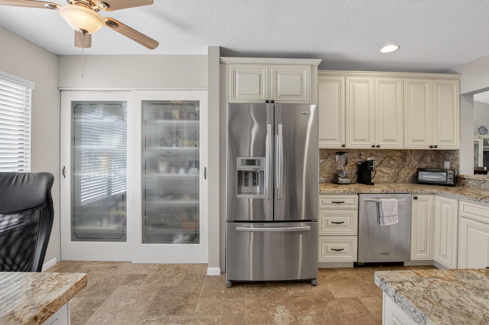 A kitchen features stainless steel appliances, off-white cabinets, granite countertops, and a frosted glass pantry — 7701 Glendevon Lane # 1907, Delray Beach FL 33446, DELRAY BEACH, FL