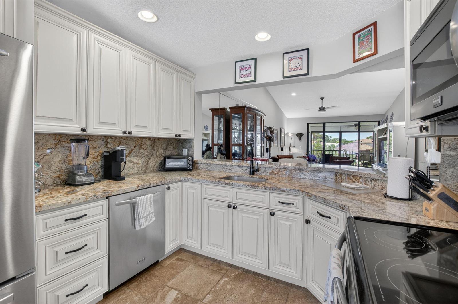 A kitchen with white cabinets, granite countertops, stainless steel appliances, and a pass-through to a living area — 7701 Glendevon Lane # 1907, Delray Beach FL 33446, DELRAY BEACH, FL