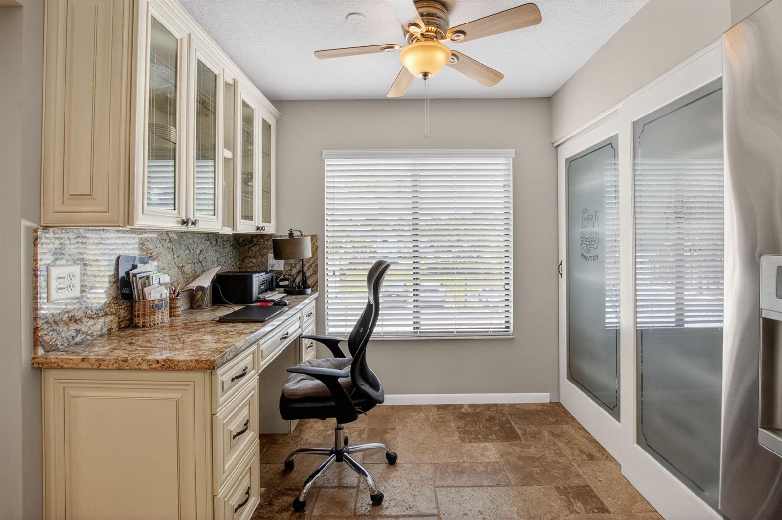 A home office features a granite desk, cream cabinetry, a ceiling fan, and pantry doors — 7701 Glendevon Lane # 1907, Delray Beach FL 33446, DELRAY BEACH, FL