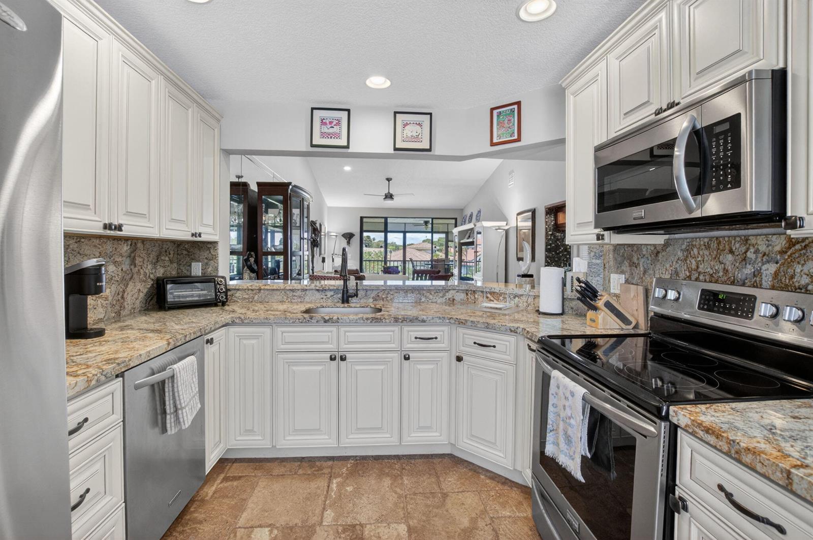 A kitchen features white cabinets, granite countertops, stainless steel appliances, and tile flooring — 7701 Glendevon Lane # 1907, Delray Beach FL 33446, DELRAY BEACH, FL