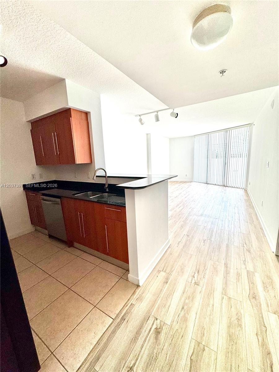 A kitchen with wood cabinets and a dark countertop overlooks an open living area — 325 S Biscayne Blvd # 1116, Miami FL 33131, MIAMI, FL
