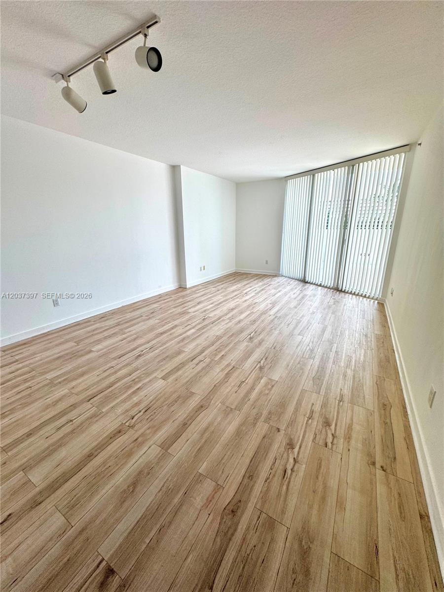 An empty room features light wood-look flooring, white walls, and vertical window blinds — 325 S Biscayne Blvd # 1116, Miami FL 33131, MIAMI, FL