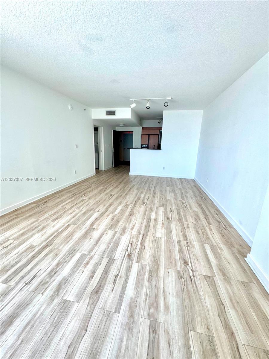 An empty living area features light wood-look flooring and a view toward the kitchen — 325 S Biscayne Blvd # 1116, Miami FL 33131, MIAMI, FL