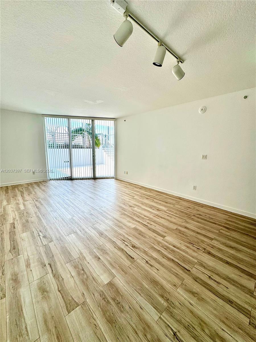 An empty room features light wood-look flooring, white walls, and a sliding glass door — 325 S Biscayne Blvd # 1116, Miami FL 33131, MIAMI, FL