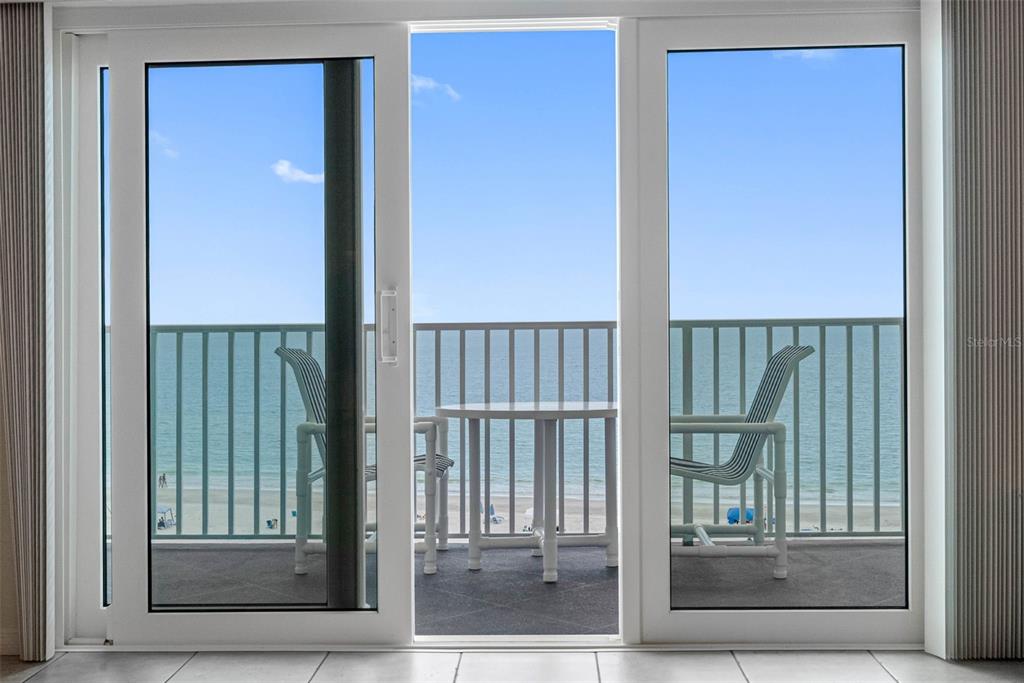 A view through sliding glass doors onto a balcony with chairs overlooking the ocean — 13500 GULF BOULEVARD UNIT 605, MADEIRA BEACH, FL
