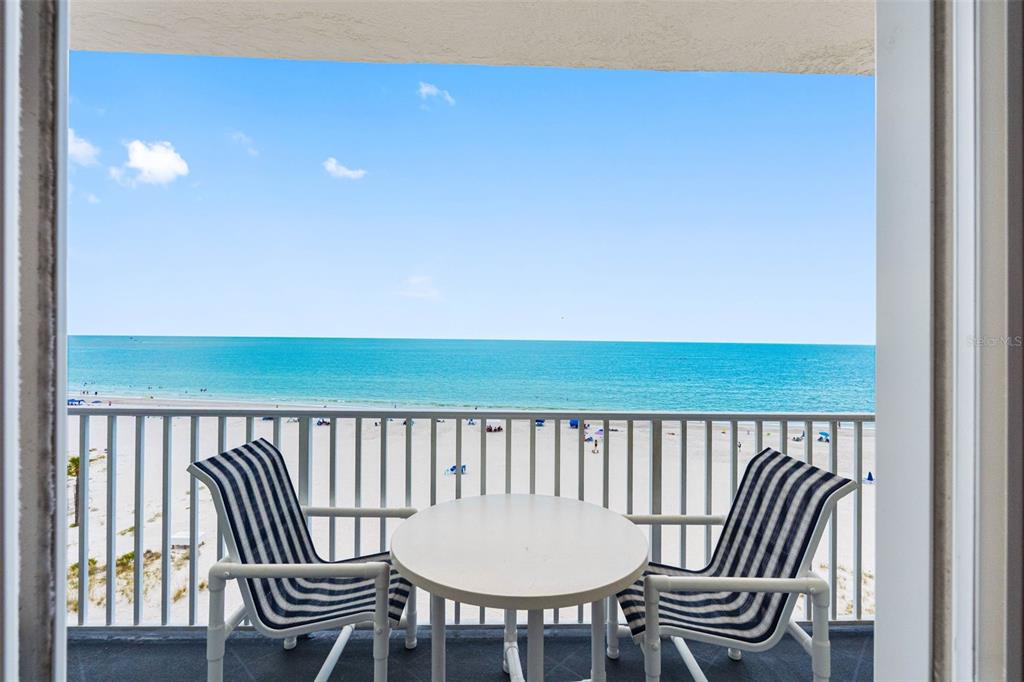A balcony with two striped chairs and a round table overlooks the beach and ocean — 13500 GULF BOULEVARD UNIT 605, MADEIRA BEACH, FL