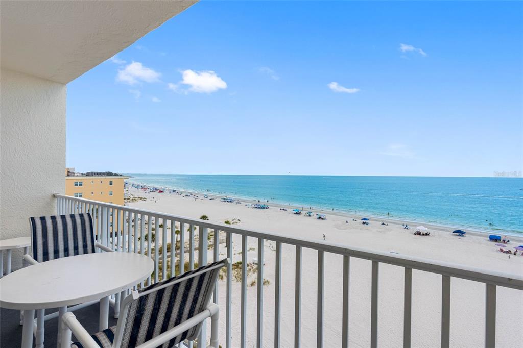 A balcony with a table and chairs overlooks a sandy beach and the ocean — 13500 GULF BOULEVARD UNIT 605, MADEIRA BEACH, FL