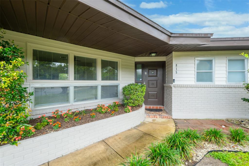 The exterior of a house features a brown front door, white brick, and a flower bed — 815 GLADE ROAD, TITUSVILLE, FL
