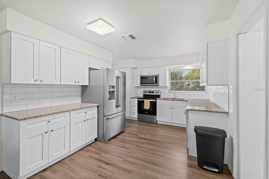 A kitchen with white cabinets, stainless steel appliances, granite countertops, and wood-look flooring — 815 GLADE ROAD, TITUSVILLE, FL
