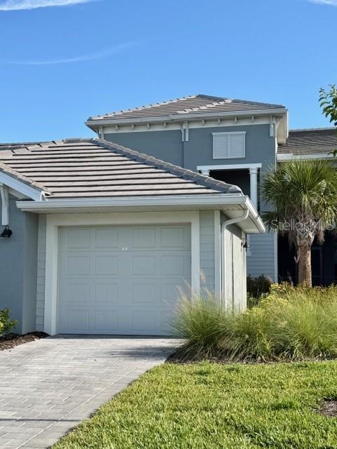 This exterior view shows a house with a gray garage door and a tiled roof — 17475 OPAL SAND DRIVE UNIT 204, VENICE, FL