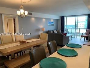 A dining area with a wooden table and chairs opens into a living room with balcony access — 6039 Collins Ave # 1131, Miami Beach FL 33140, MIAMI BEACH, FL