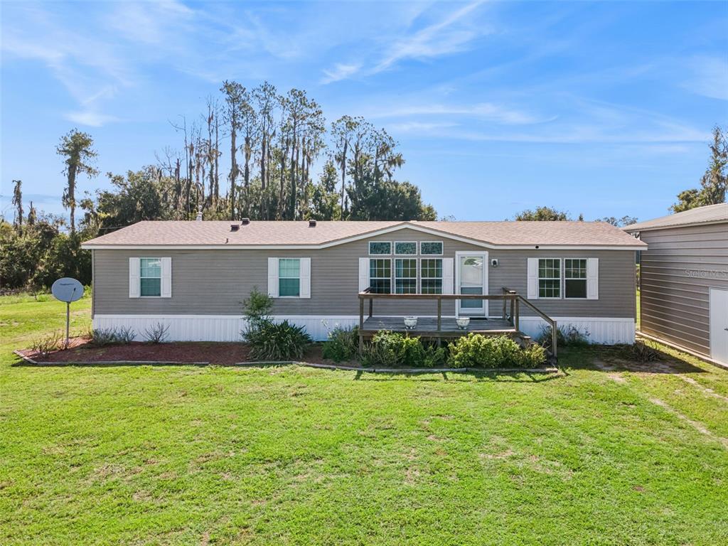 A single-story manufactured home with grey siding, a wooden deck, and a metal storage building — 1153 SAND MOUNTAIN ROAD, FORT MEADE, FL