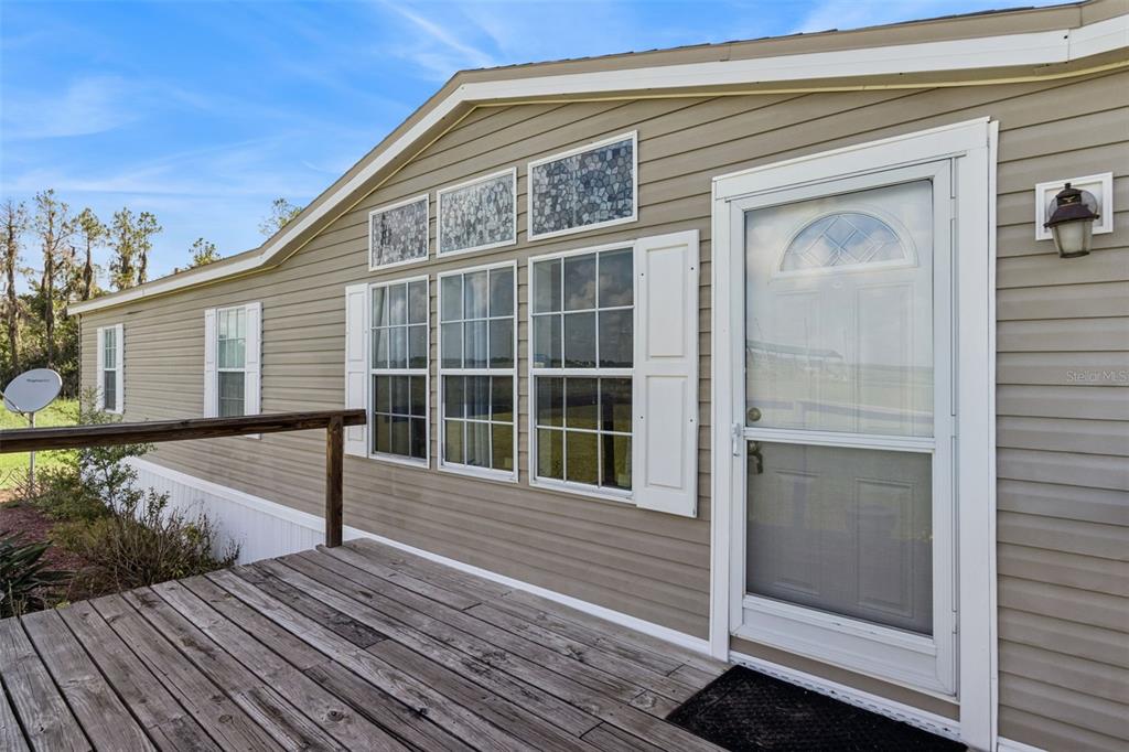A tan-sided mobile home exterior features a wooden deck, white shutters, and stained-glass accents — 1153 SAND MOUNTAIN ROAD, FORT MEADE, FL