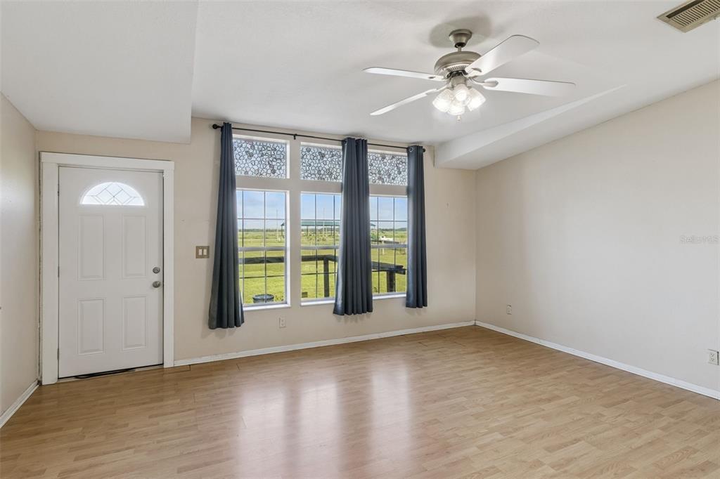A living room features light wood flooring, a ceiling fan, and windows with blue curtains — 1153 SAND MOUNTAIN ROAD, FORT MEADE, FL