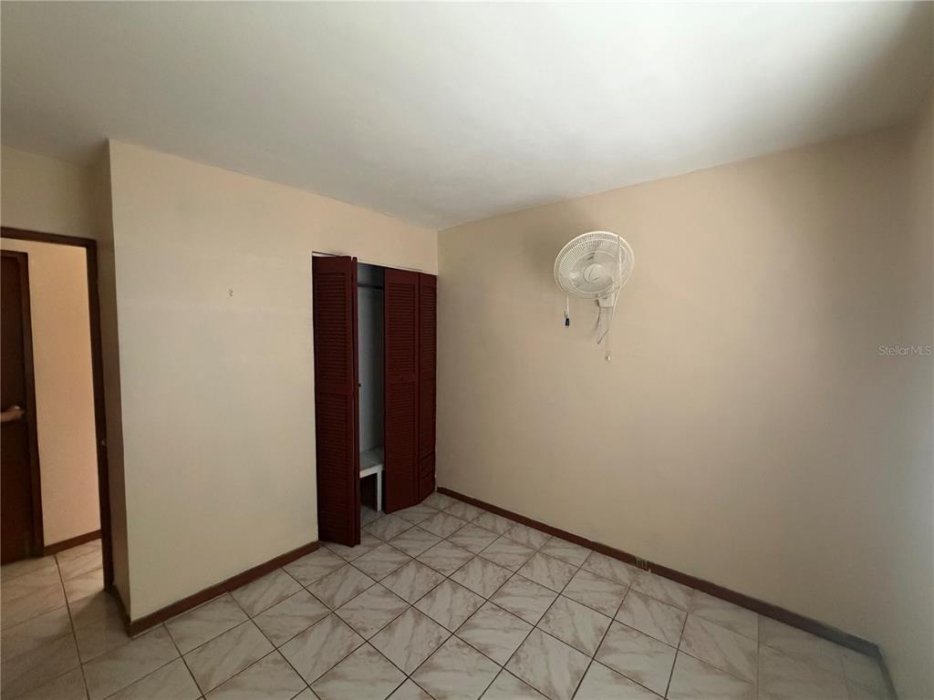 A bedroom features beige walls, tiled flooring, a wall-mounted fan, and a louvered closet door — 1 ANTONIO DE GRACIA, TOA ALTA, PR