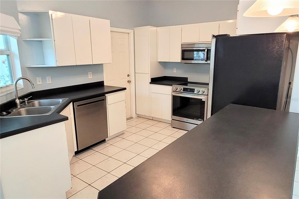 A kitchen features white cabinets, black countertops, stainless steel appliances, and light-colored floor tiles — 2354 TAMI SOLA STREET, SARASOTA, FL