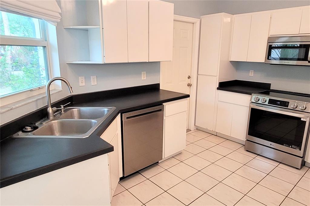A kitchen features white cabinets, black countertops, stainless steel appliances, and light-colored tile flooring — 2354 TAMI SOLA STREET, SARASOTA, FL