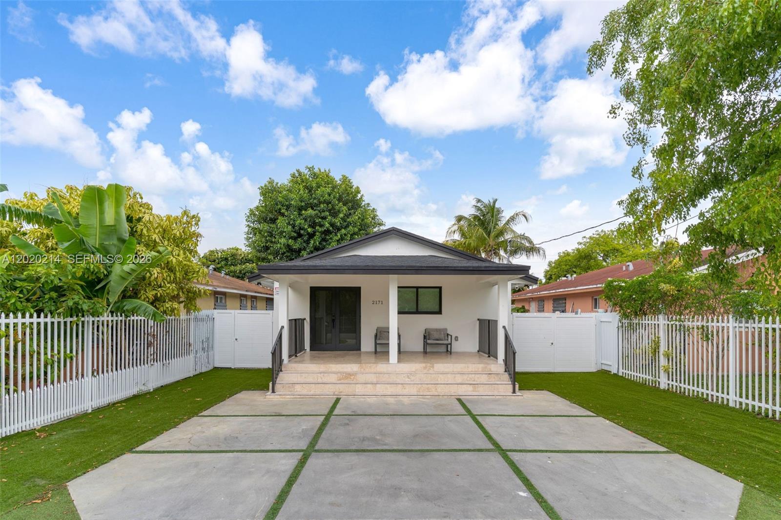A single-story house with a concrete driveway, white picket fence, and a covered front porch — 2171 NW 49th St, Miami FL 33142, MIAMI, FL