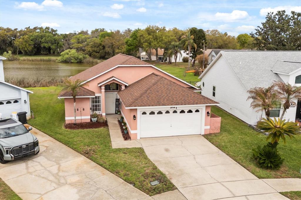 An aerial view shows a peach-colored house with a two-car garage and a lake — 3114 DELLCREST PLACE, LAKE MARY, FL