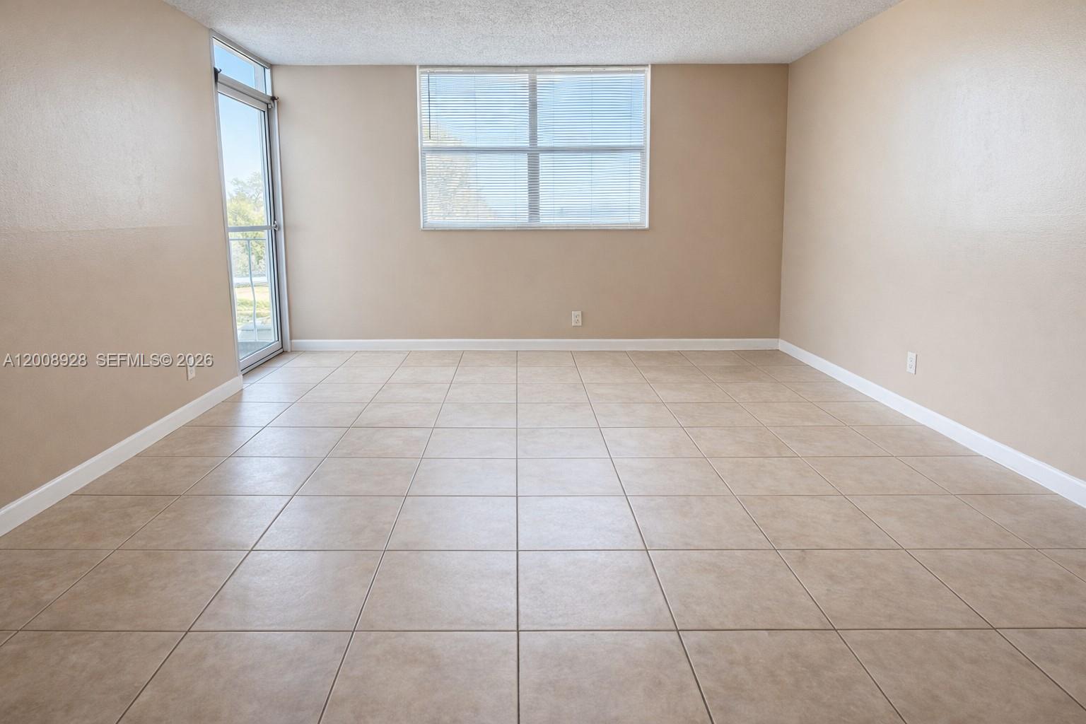 An empty room features beige walls, large square floor tiles, a window, and a door — 470 Executive Center Dr # 2D, West Palm Beach FL 33401, WEST PALM BEACH, FL