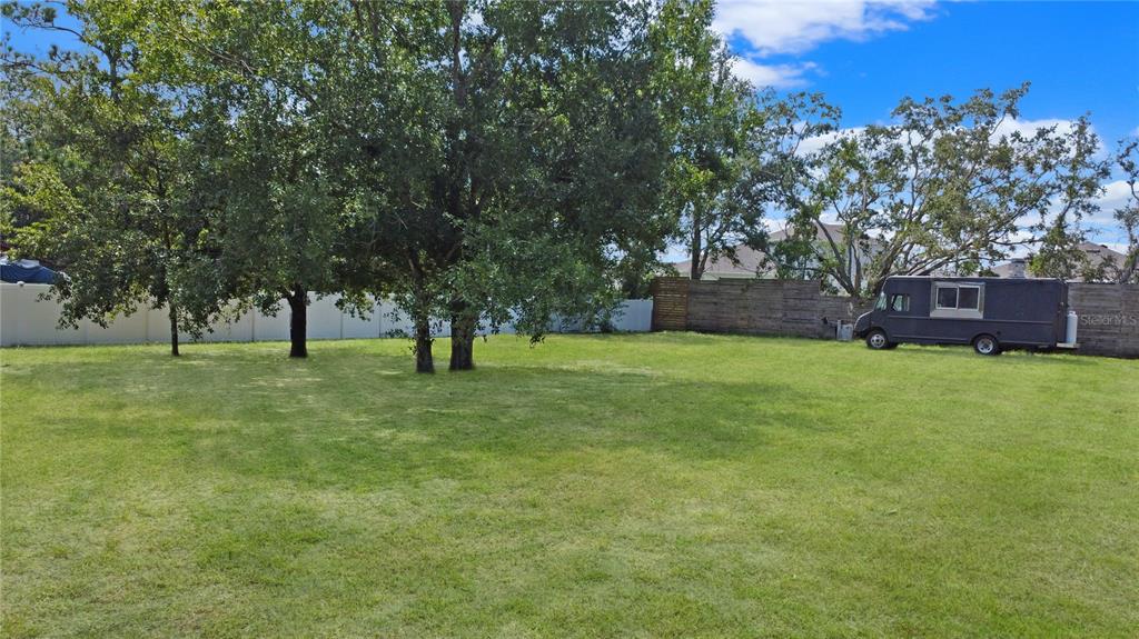 A large, grassy backyard features several mature trees, a white fence, and a dark trailer — CITRUS STREET, KISSIMMEE, FL