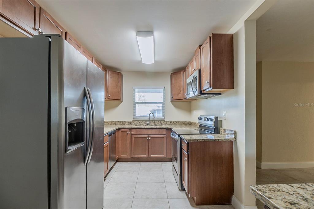 A kitchen features stainless steel appliances, wood cabinets, granite countertops, and light-colored tile flooring — 4320 MEADOWBROOK AVENUE, ORLANDO, FL