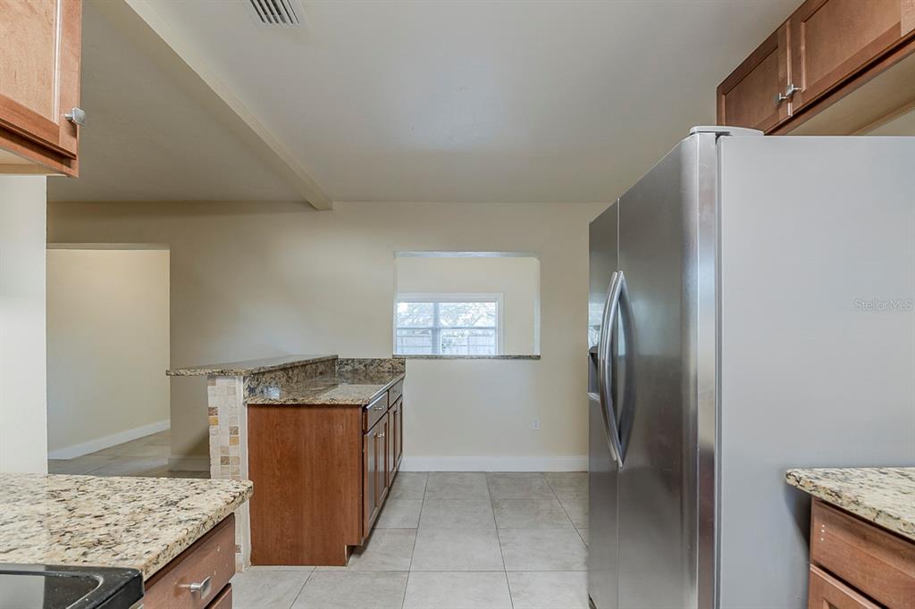 A kitchen features wood cabinets, granite countertops, tile flooring, and a stainless steel refrigerator — 4320 MEADOWBROOK AVENUE, ORLANDO, FL