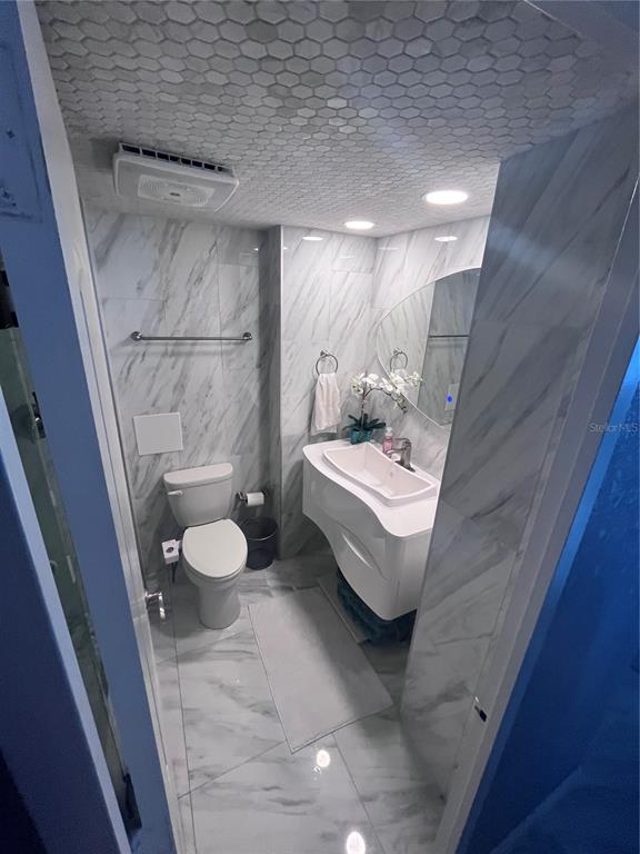 A bathroom features marble-look tile walls, a hexagonal tiled ceiling, and a modern vanity — 880 MANDALAY AVENUE UNIT S302, CLEARWATER BEACH, FL