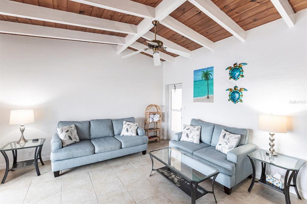 A living room features two blue sofas, a glass coffee table, and a wood-paneled ceiling — 6006 MIDNIGHT PASS ROAD UNIT 5, SARASOTA, FL