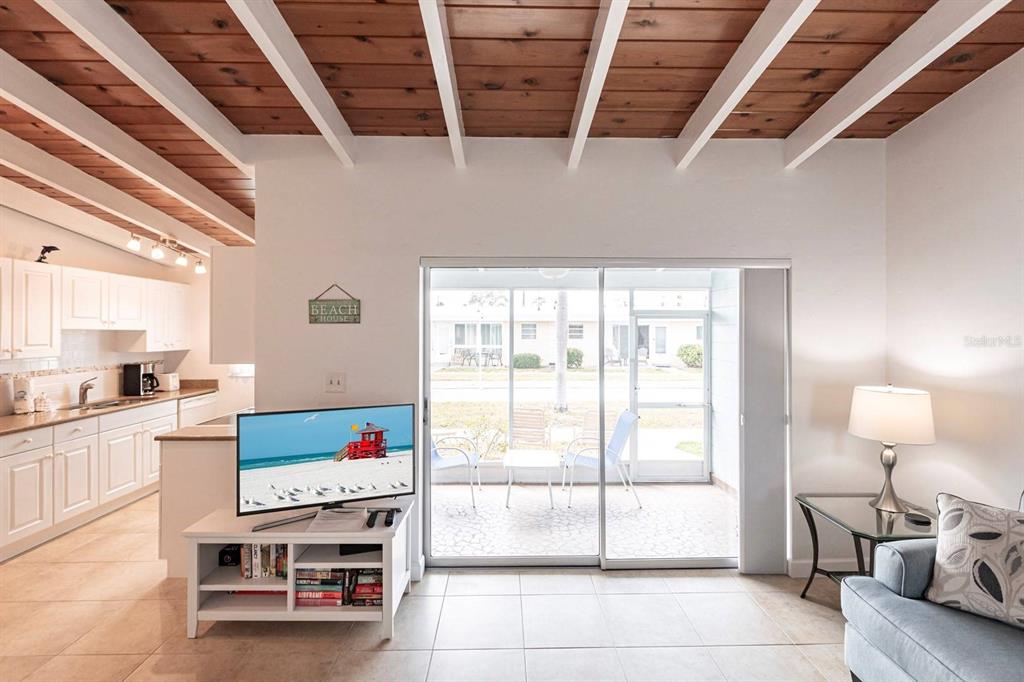 A living room with a wood-beamed ceiling, tile floors, and a sliding door to a patio — 6006 MIDNIGHT PASS ROAD UNIT 5, SARASOTA, FL