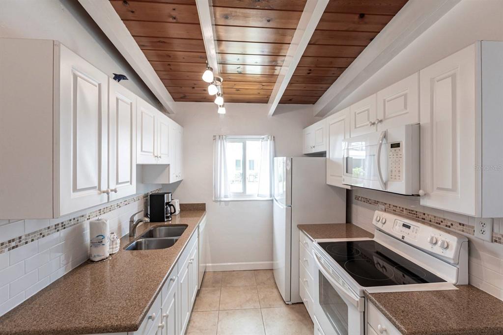A galley kitchen features white cabinets, brown countertops, and a wood-paneled ceiling with track lighting — 6006 MIDNIGHT PASS ROAD UNIT 5, SARASOTA, FL