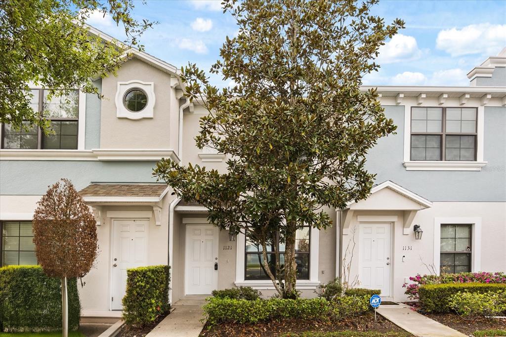 A two-story townhouse exterior features light blue siding, white trim, and a central tree — 1121 TRILLIUM PARK LANE, SANFORD, FL