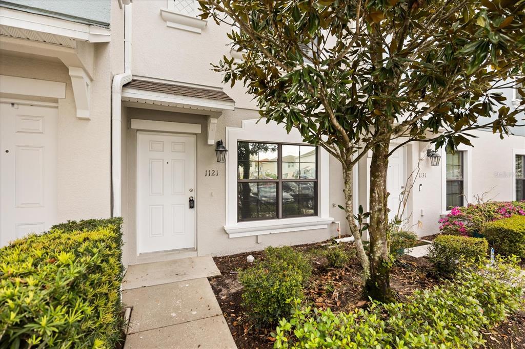 A white townhome exterior features a front door, a window, and a small front yard — 1121 TRILLIUM PARK LANE, SANFORD, FL